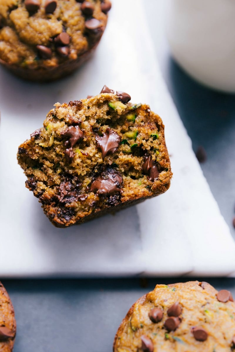 Gluten free zucchini muffins, with one split open to show the insides revealing the fluffy muffin, zucchini, and melted chocolate chips.