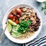 A bowl filled with honey-lime chicken served with quinoa, tomatoes, avocados, and black beans, creating a flavorful and wholesome meal.