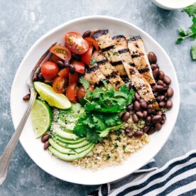 A bowl filled with honey-lime chicken served with quinoa, tomatoes, avocados, and black beans, creating a flavorful and wholesome meal.
