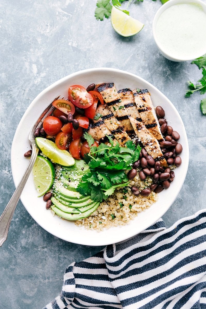 A bowl filled with honey-lime chicken served with quinoa, tomatoes, avocados, and black beans, creating a flavorful and wholesome meal.