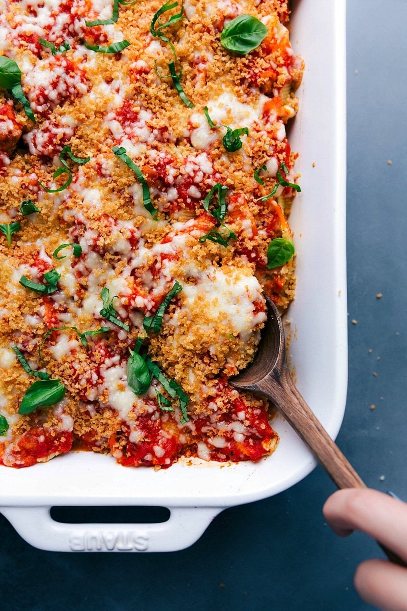 Overhead view of the finished Chicken Parm Stuffed Shells, with someone scooping out a serving.