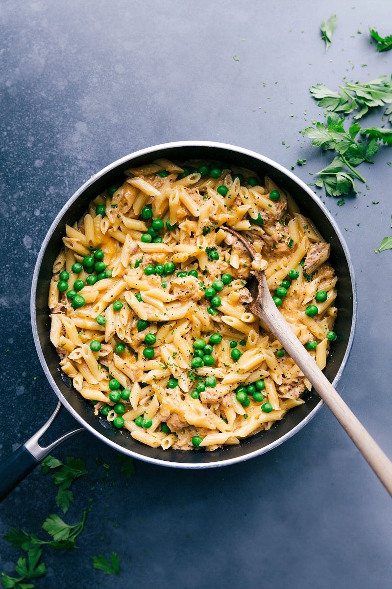 Tuna pasta in a skillet with peas and cheese, creating a savory and hearty meal.