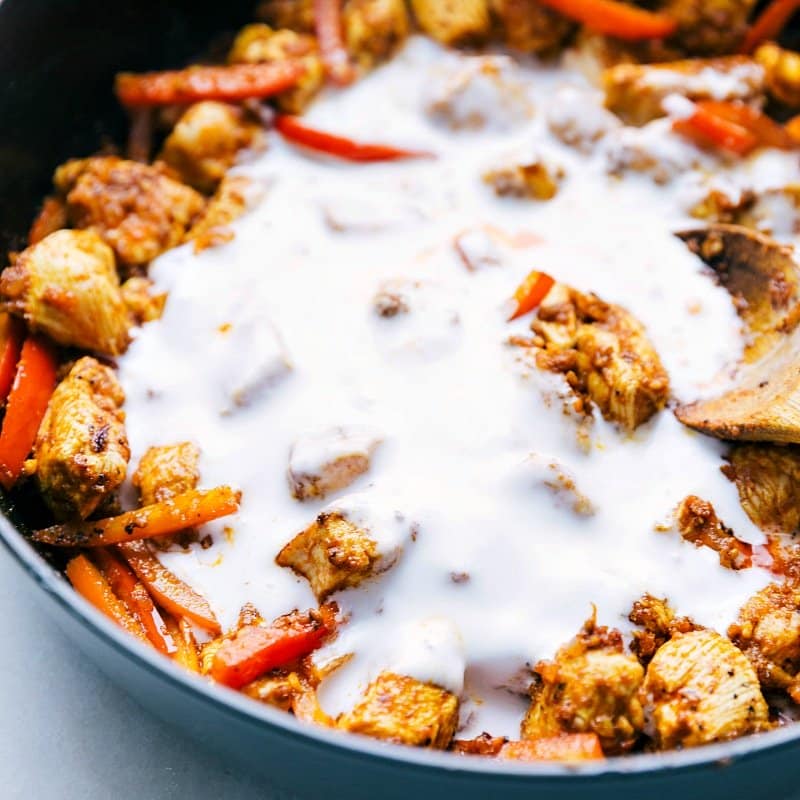 Coconut milk being added to the chicken and red peppers in the pan, creating a creamy base for chicken curry with coconut milk.