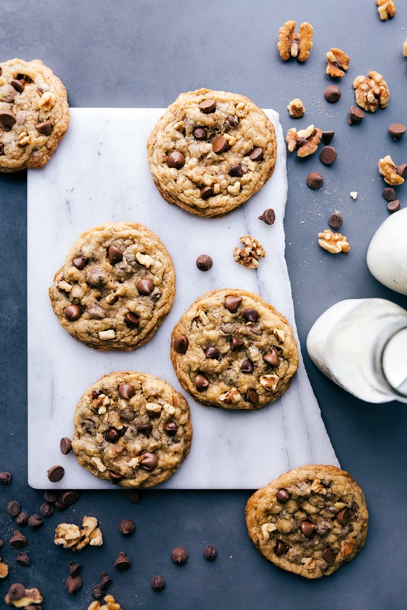 Overhead view of baked DoubleTree Cookies with milk, walnuts and chocolate chips nearby.