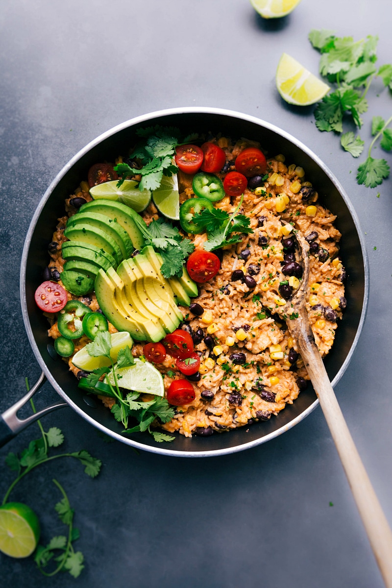 Mexican Chicken and Rice in the skillet, topped with fresh vegetables ready to be mixed in, and all set to be enjoyed.