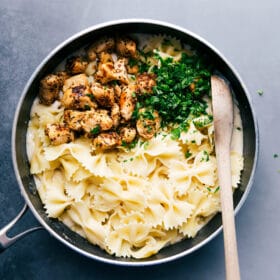 Pasta, chicken, and fresh parsley over the alfredo sauce, about to be mixed together to create a delicious meal.