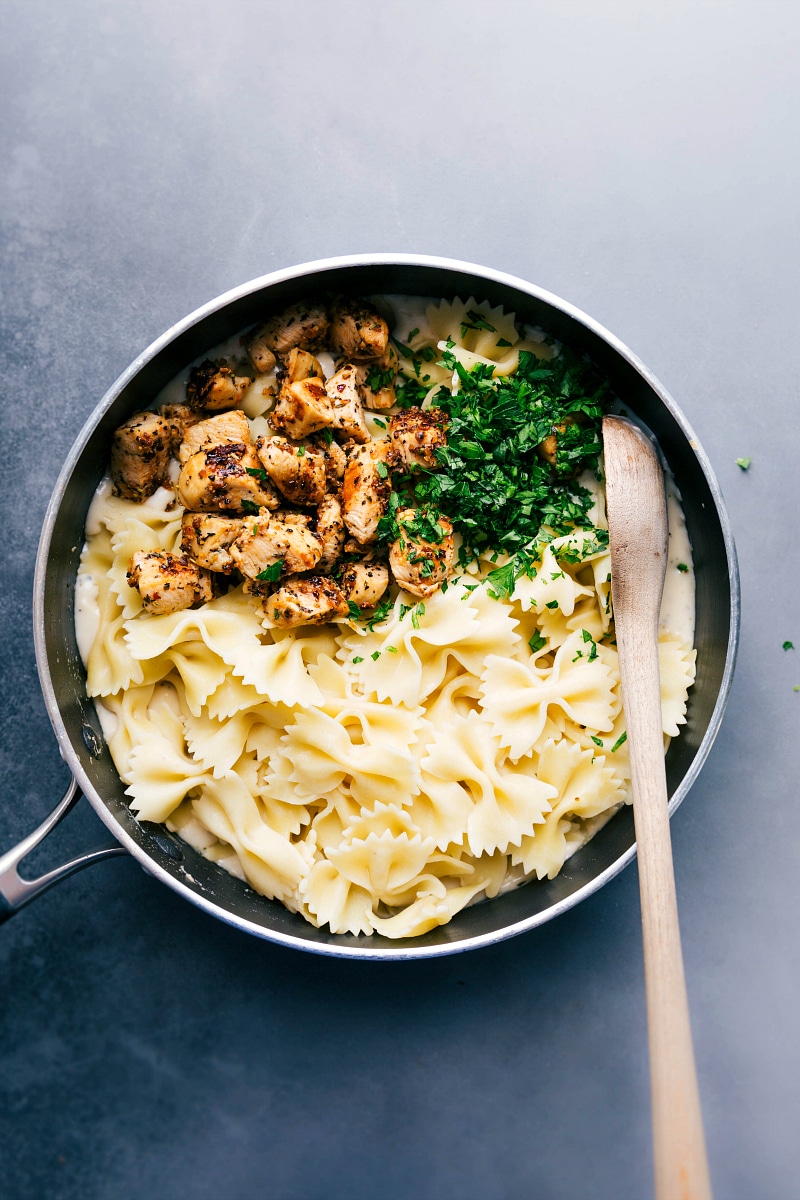 Overhead image of pasta, chicken, and fresh parsley over the Alfredo sauce, about to be mixed together.