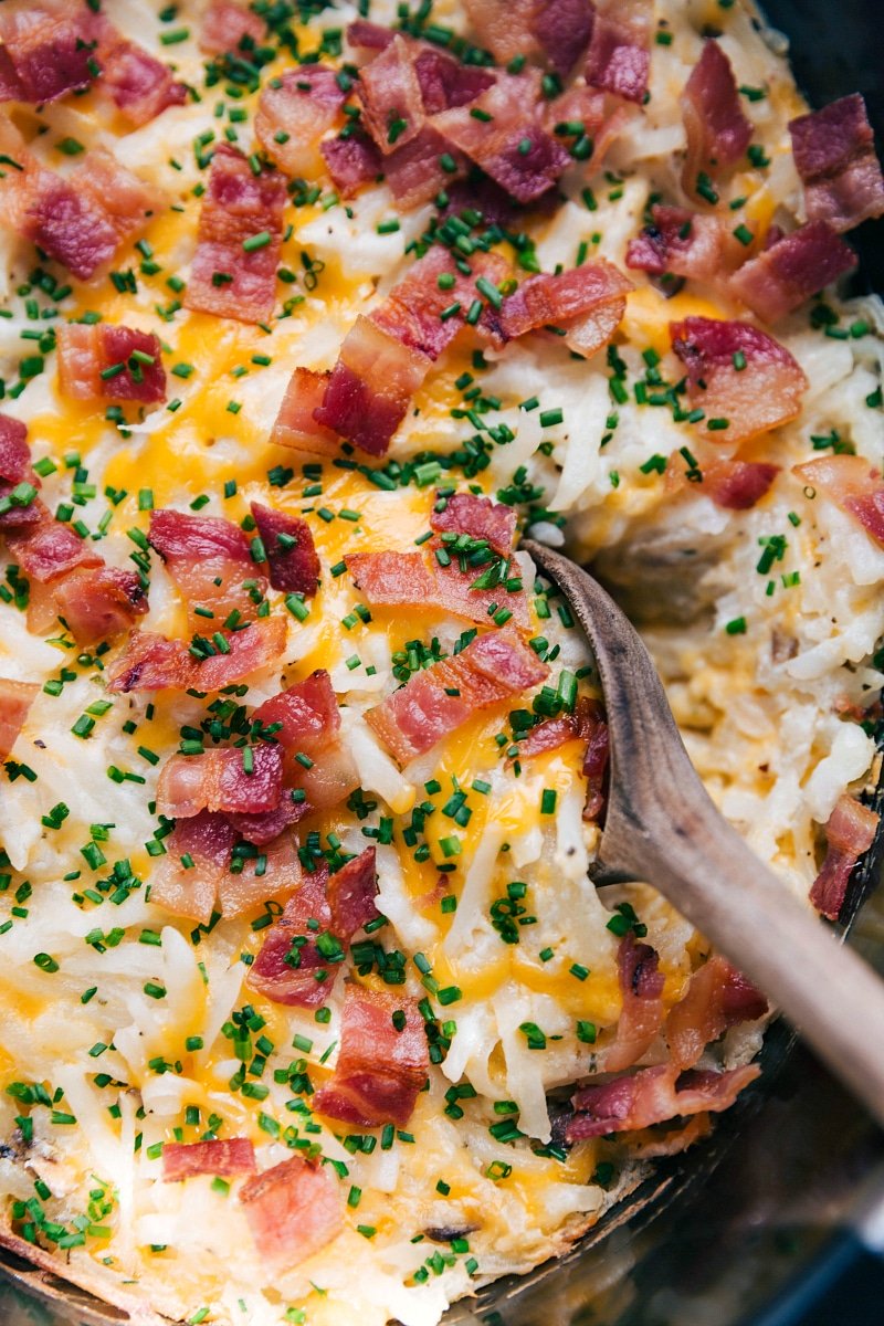 Close-up view of Crockpot Hashbrown Casserole, with a wooden spoon scooping up a serving.