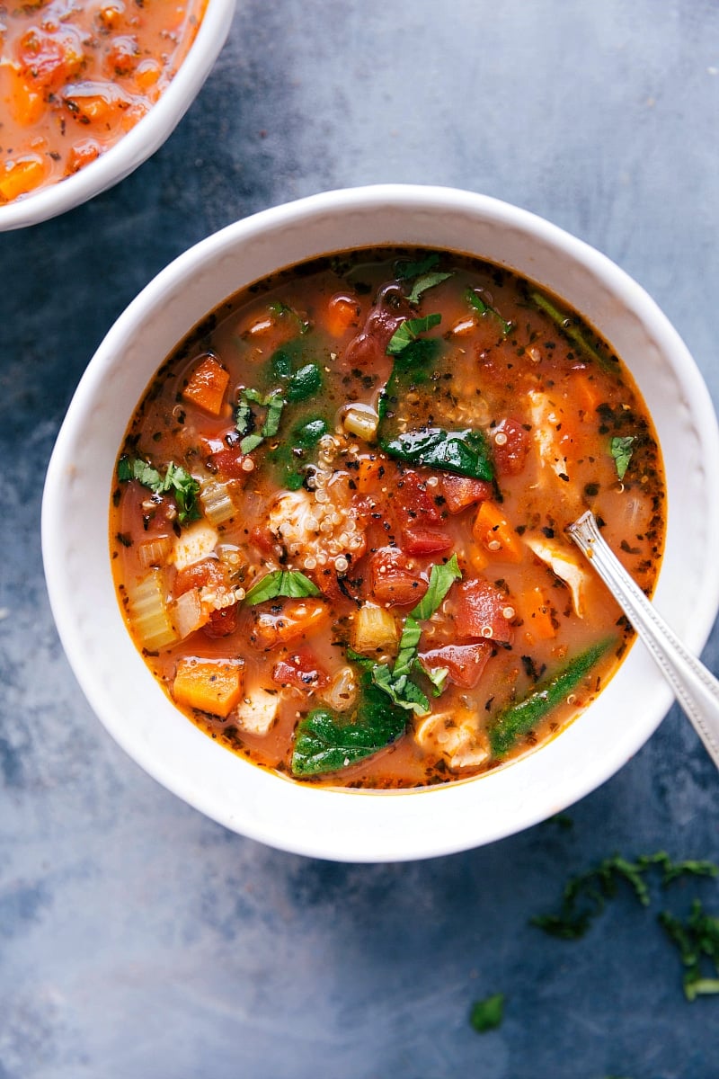 A bowl of hearty crockpot chicken quinoa soup, with chicken, quinoa, vegetables, and herbs.