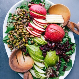 Quinoa apple salad on a platter with fresh greens, sliced apples, nuts, and more.