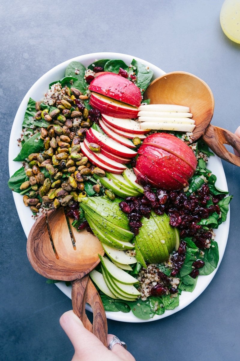 Quinoa apple salad on a platter with fresh greens, sliced apples, nuts, and more.