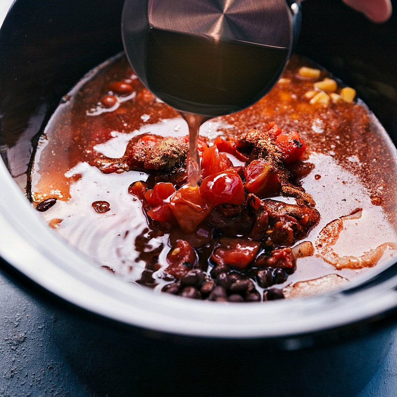 Chicken stock being poured into the slow cooker for the crockpot vegetarian chili with quinoa.