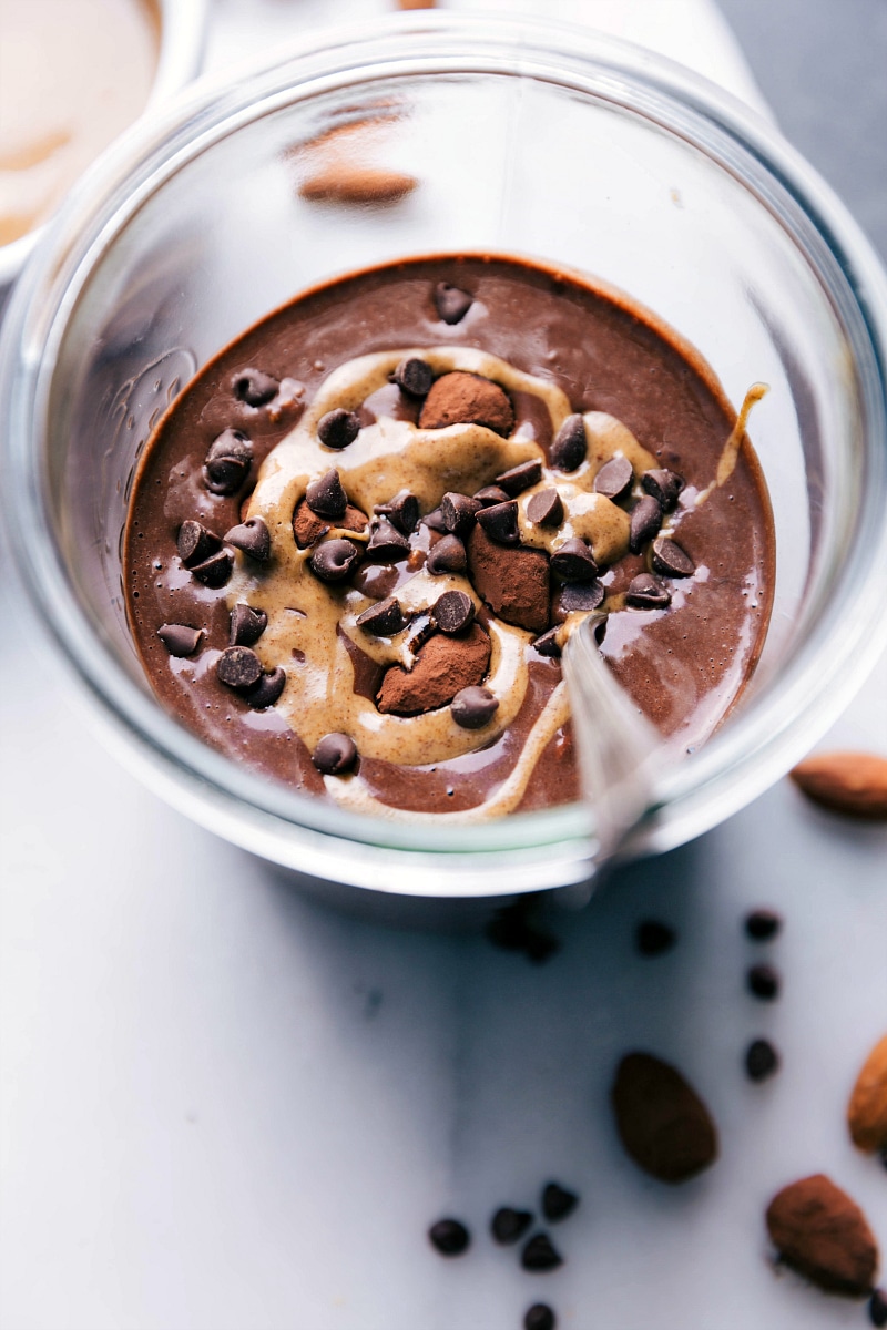 Delicious overnight oats made with chocolate almond milk, ready to eat, topped with a beautiful almond butter swirl and chocolate chips.