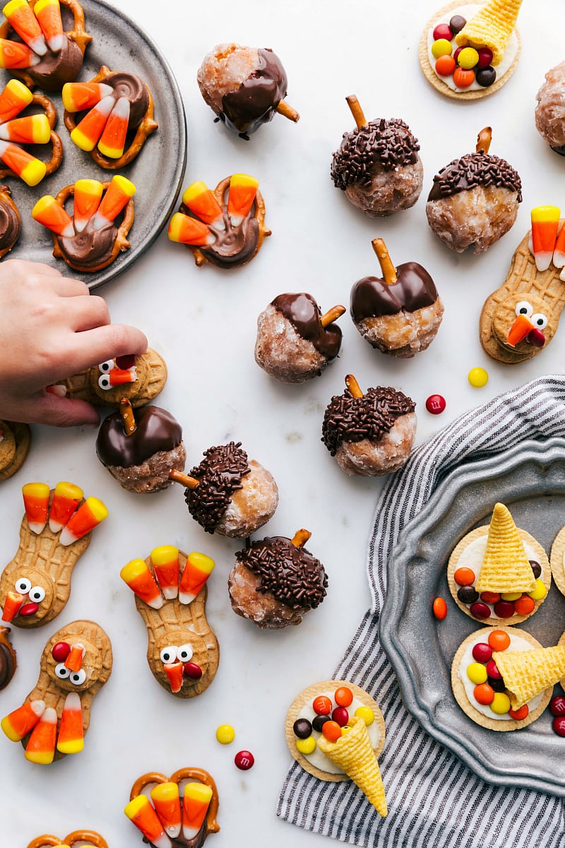 Fall treats on a board, showing the acorn donut holes, as well as turkey nutter butter treats, turkey pretzel rolo treats, and bugle cornucopia.