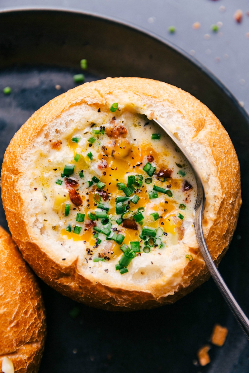 Savory baked potato soup topped with fresh herbs and melted cheese in a bread bowl, ready to be devoured.