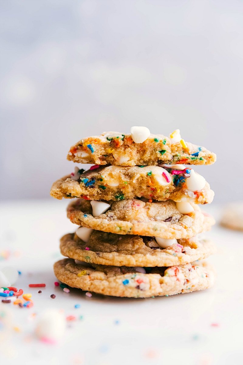 A stack of cake batter cookies, with one cookie broken open to reveal its delicious interior, and all of them topped with colorful sprinkles for a delightful treat.