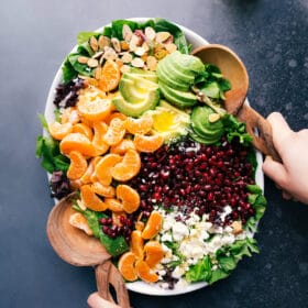 Fresh ingredients for the orange pomegranate salad in a bowl including orange slices, pomegranate seeds, mixed greens, walnuts, and feta cheese, ready for mixing.