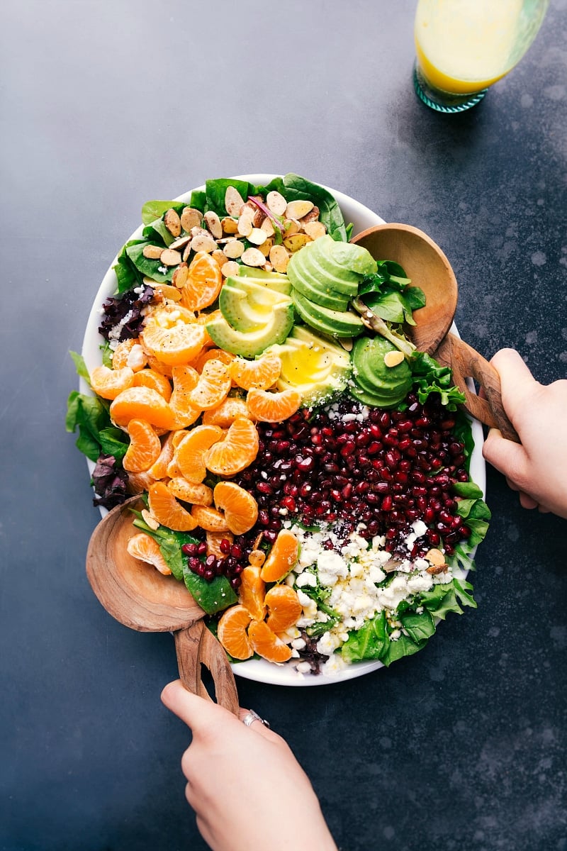 Fresh ingredients for the orange pomegranate salad in a bowl including orange slices, pomegranate seeds, mixed greens, walnuts, and feta cheese, ready for mixing.