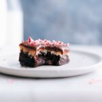 A luscious peppermint brownie with a bite mark, showcasing its peppermint frosting and rich chocolate ganache topping, presented on a plate.