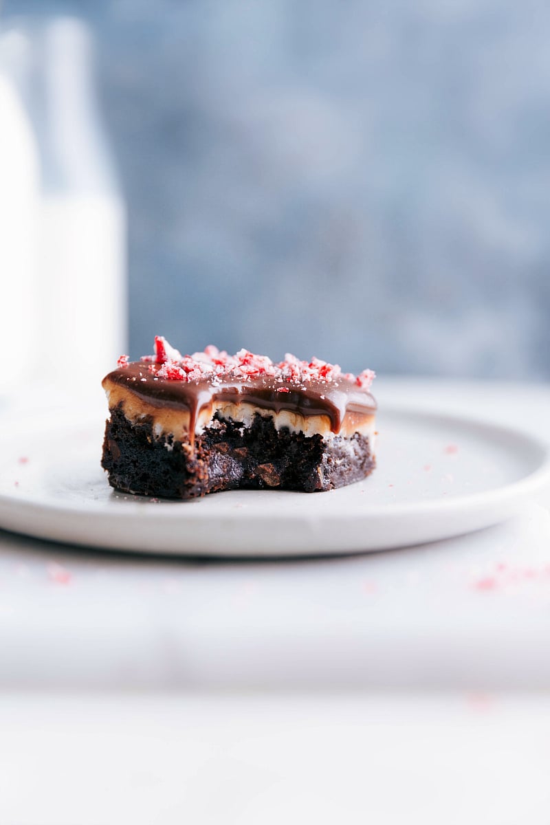 A luscious peppermint brownie with a bite mark, showcasing its peppermint frosting and rich chocolate ganache topping, presented on a plate.