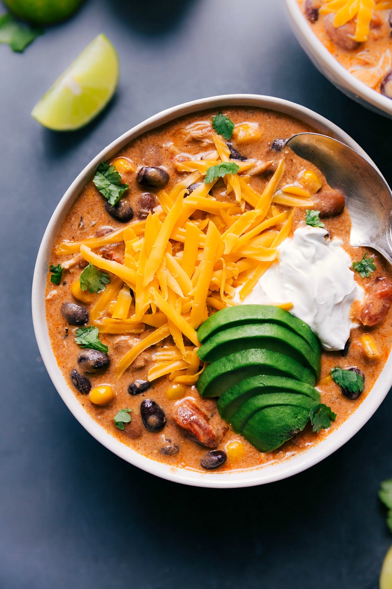 A bowl of the finished chicken chili recipe, adorned with shredded cheese, sour cream, and avocado toppings, offering a creamy and flavorful meal.