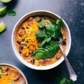 A bowl filled with warm chicken chili, generously topped with cheese, avocado slices, and fresh herbs, presenting a comforting and flavorful dish.