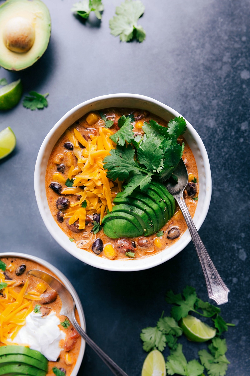 A bowl filled with warm chicken chili, generously topped with cheese, avocado slices, and fresh herbs, presenting a comforting and flavorful dish.