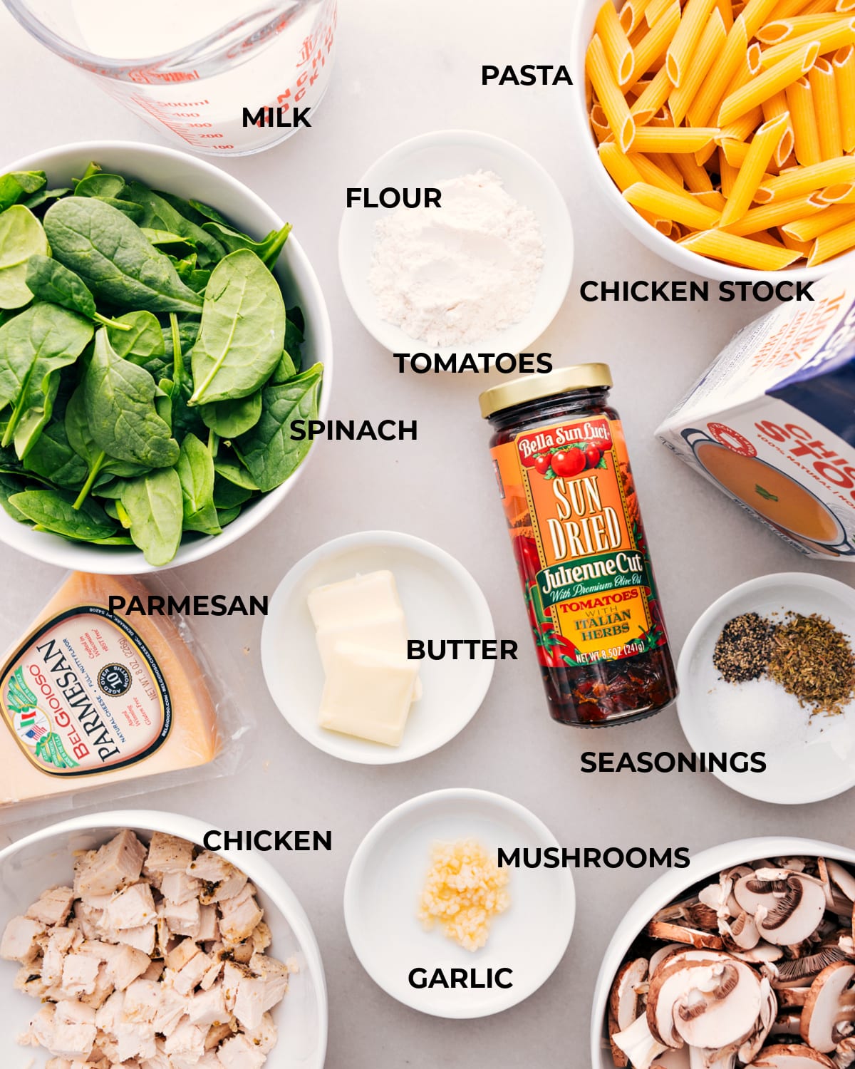 Ingredients for Chicken Penne Pasta, including measured portions of chicken, penne, cheese, sun-dried tomatoes, mushrooms and spinach, are neatly laid out.