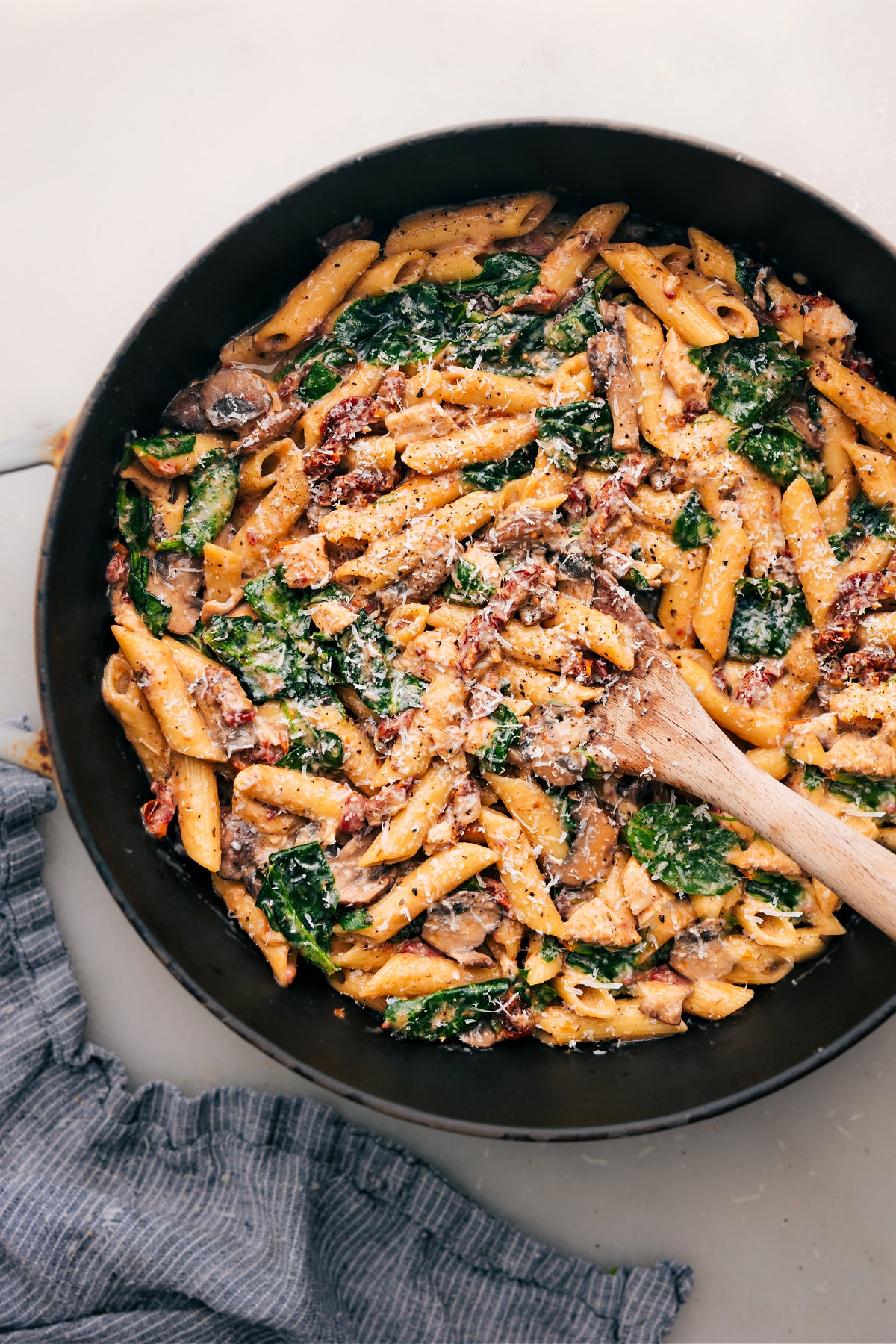 A pot of warm chicken penne pasta features melted cheese, sun-dried tomatoes, and fresh spinach, ready to be served.