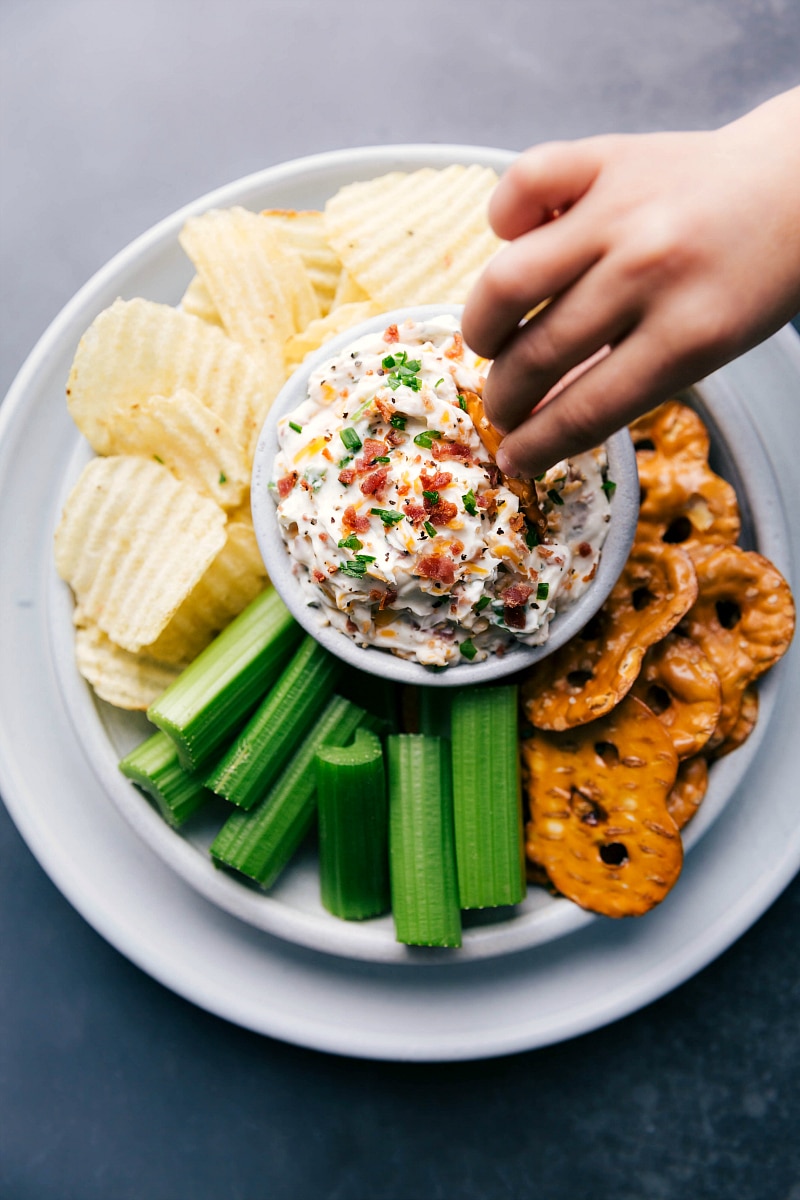 Overhead view of a hand dipping a pretzel into a bowl of Baked Potato Dip.