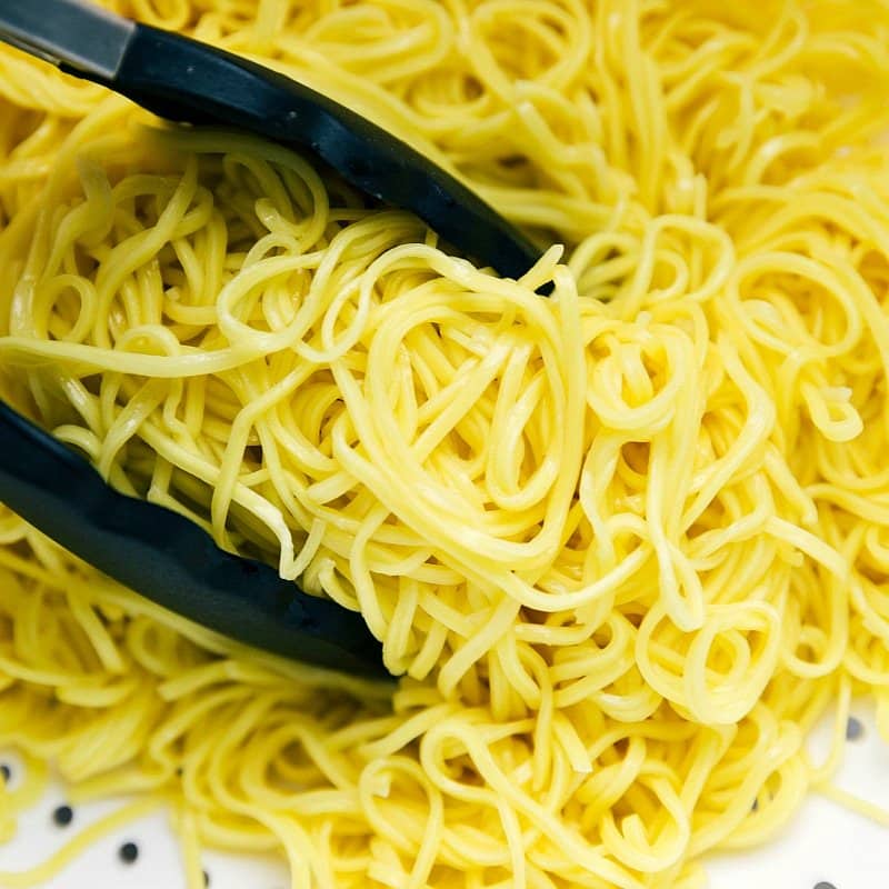 Drained chow mein noodles being picked up with tongs.