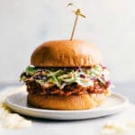 Crockpot BBQ pulled pork sandwich on a plate, overflowing with delicious ingredients, ready to be enjoyed.