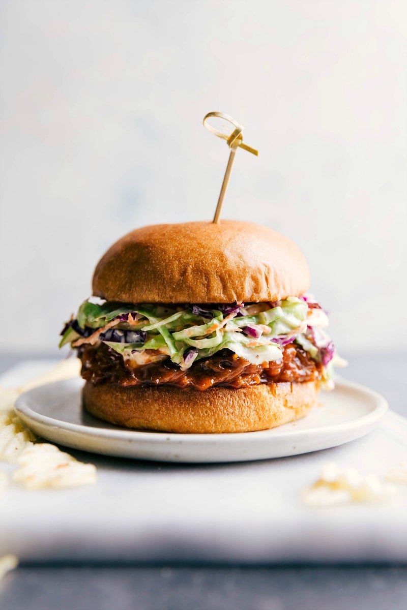 Crockpot BBQ pulled pork sandwich on a plate, overflowing with delicious ingredients, ready to be enjoyed.