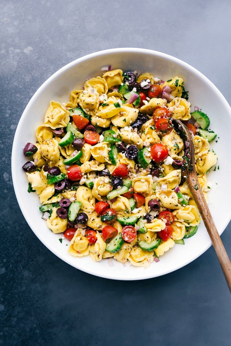 Greek tortellini salad with a spoon in the bowl, ready to be served with fresh vegetables and delicious dressing.