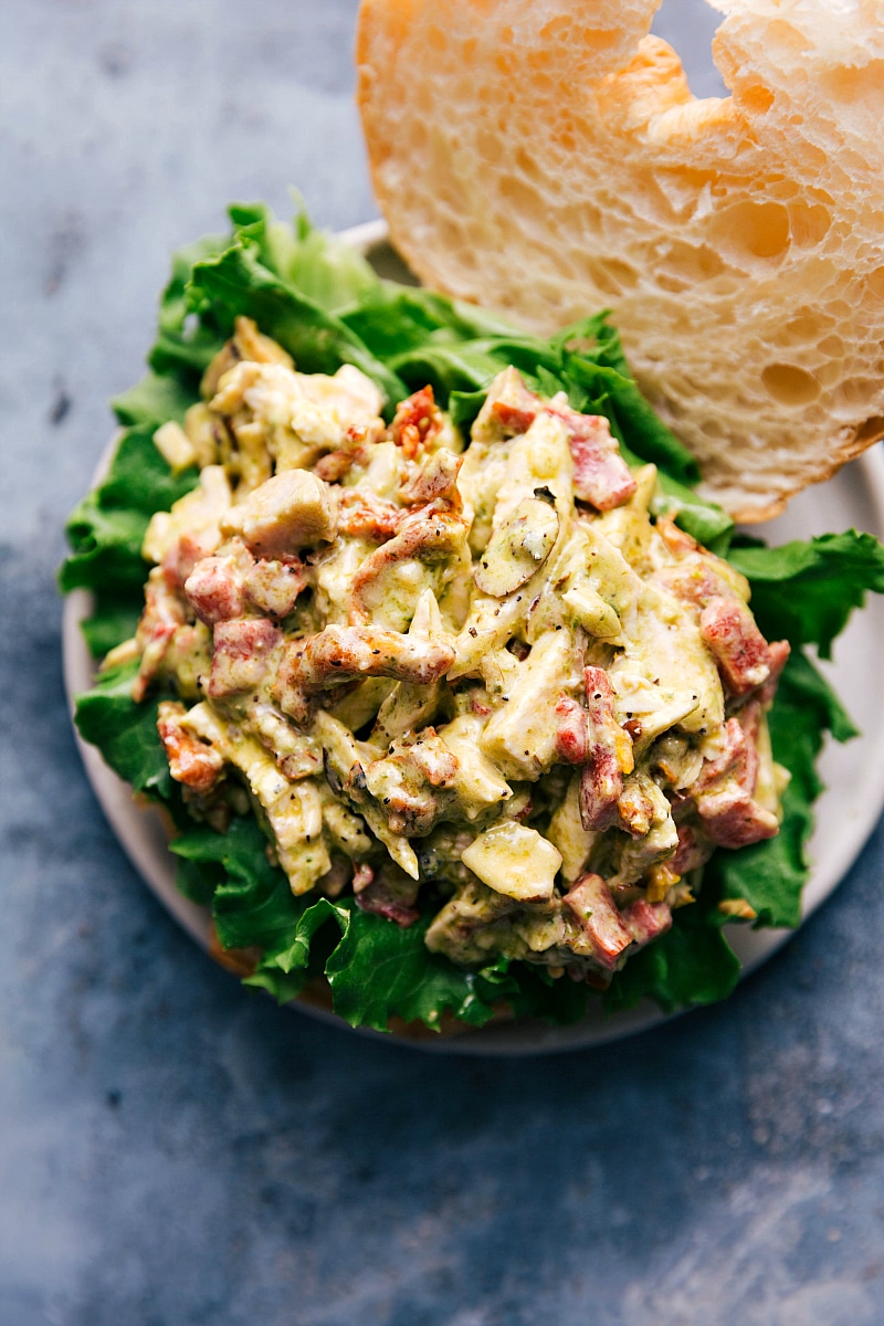 Pesto chicken salad served in a croissant bun, resting on a bed of fresh lettuce.