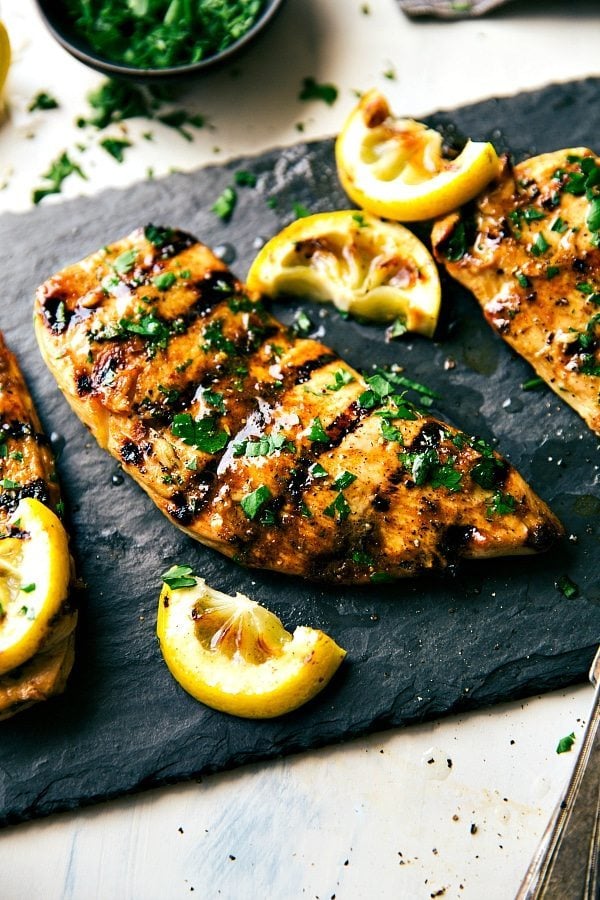 The best grilled chicken marinade, garnished with fresh herbs on top and lemon juice ready to be cut up and enjoyed for added flavor.