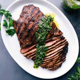 A sizzling grilled flank steak with a drizzle of vibrant chimichurri sauce on top.