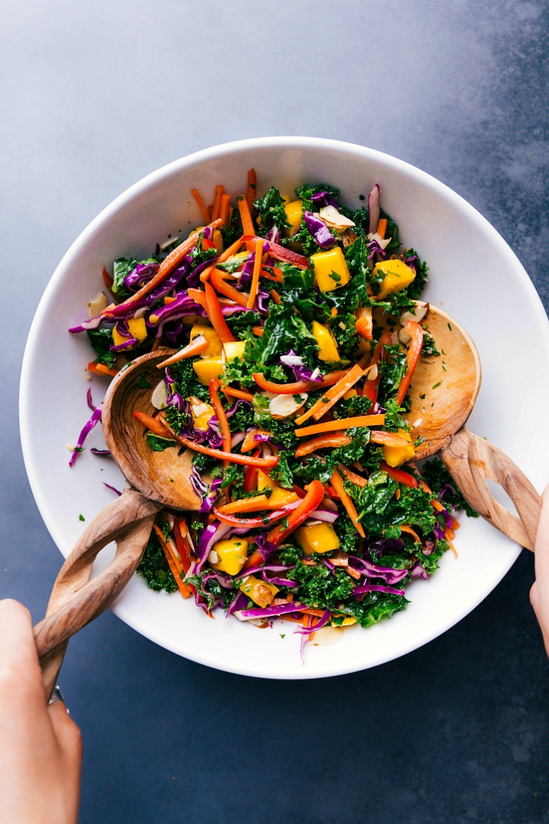 Finished colorful kale salad recipes being scooped with wooden spoons, ready for serving.