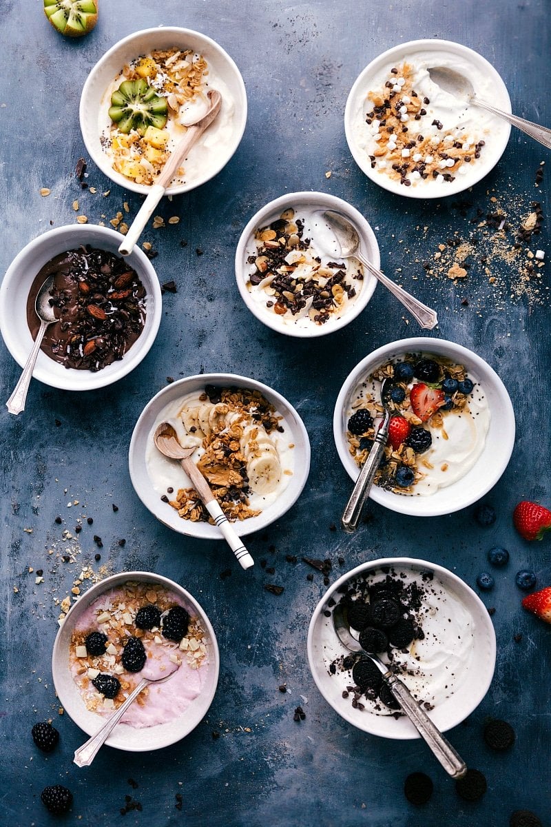 Overhead image of eight different Yogurt Bowls with spoons in them ready to be eaten.