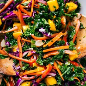 Colorful bowl of the completed kale salad recipe, complete with wooden serving spoons.