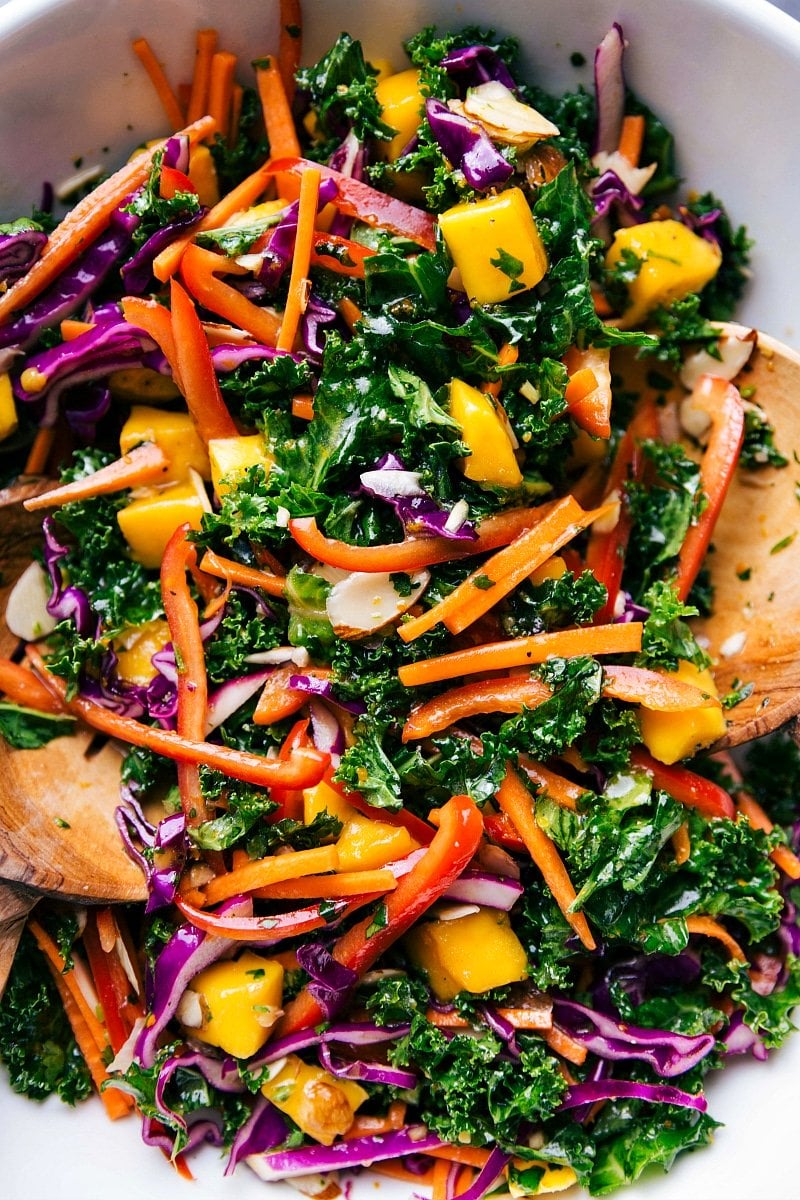 Colorful bowl of the completed kale salad recipe, complete with wooden serving spoons.