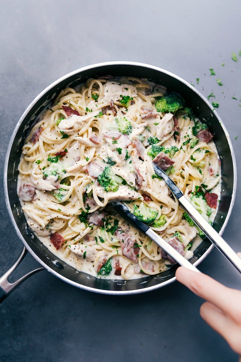 Chicken broccoli alfredo with tongs scooping up a creamy and delicious bite, ready to be enjoyed.