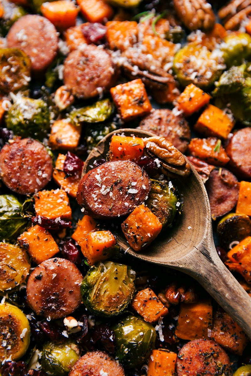 Harvest sausage and vegetables, with a spoonful being scooped up and topped with cheese.