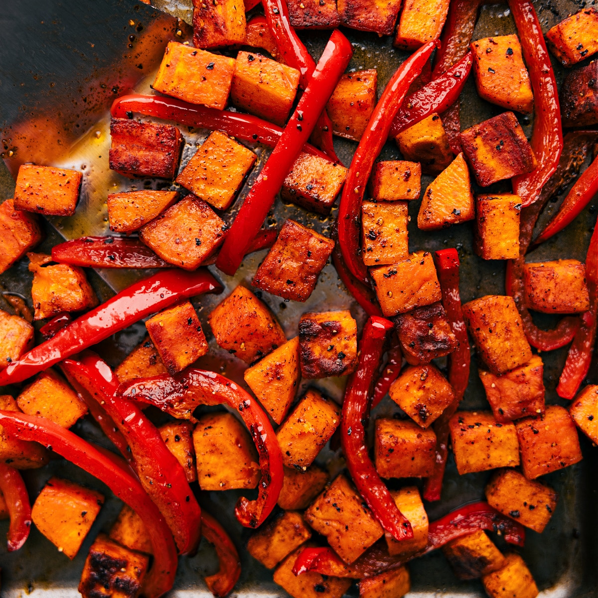 Tray of freshly roasted potatoes and peppers, golden brown and sizzling straight out of the oven.