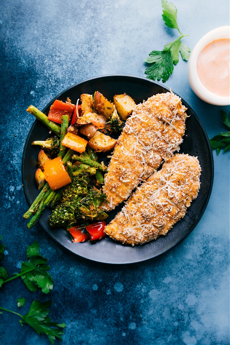 Overhead image of the baked parmesan chicken tenders on a plate with veggies on the side