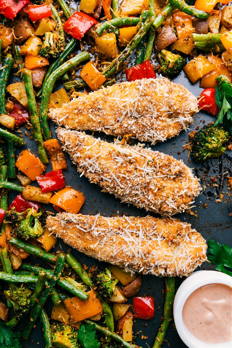 Overhead image of the baked parmesan chicken tenders fresh out of the oven with veggies surrounding it