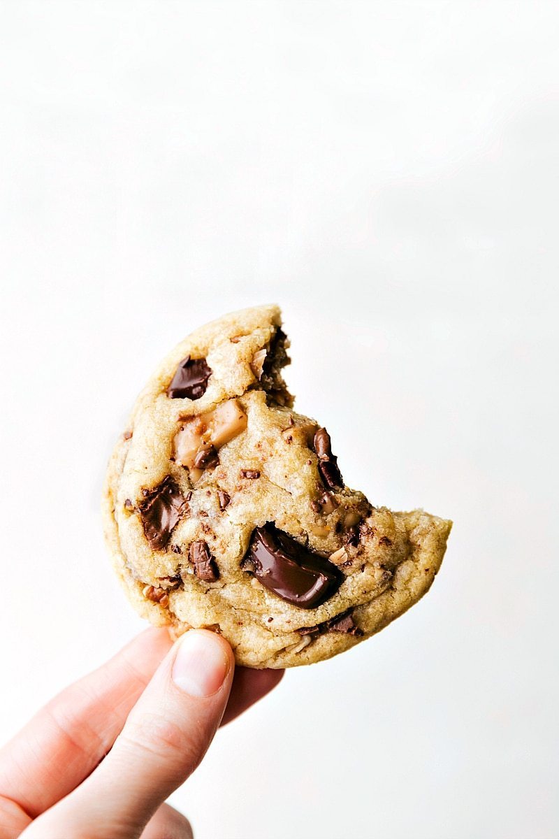 Image of a Toffee Cookie being held with a bite out of it.