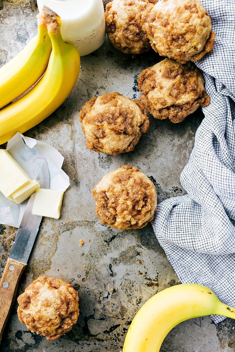 Banana muffins with crumb topping presented with fresh bananas and a container of milk, a delicious breakfast or snack.
