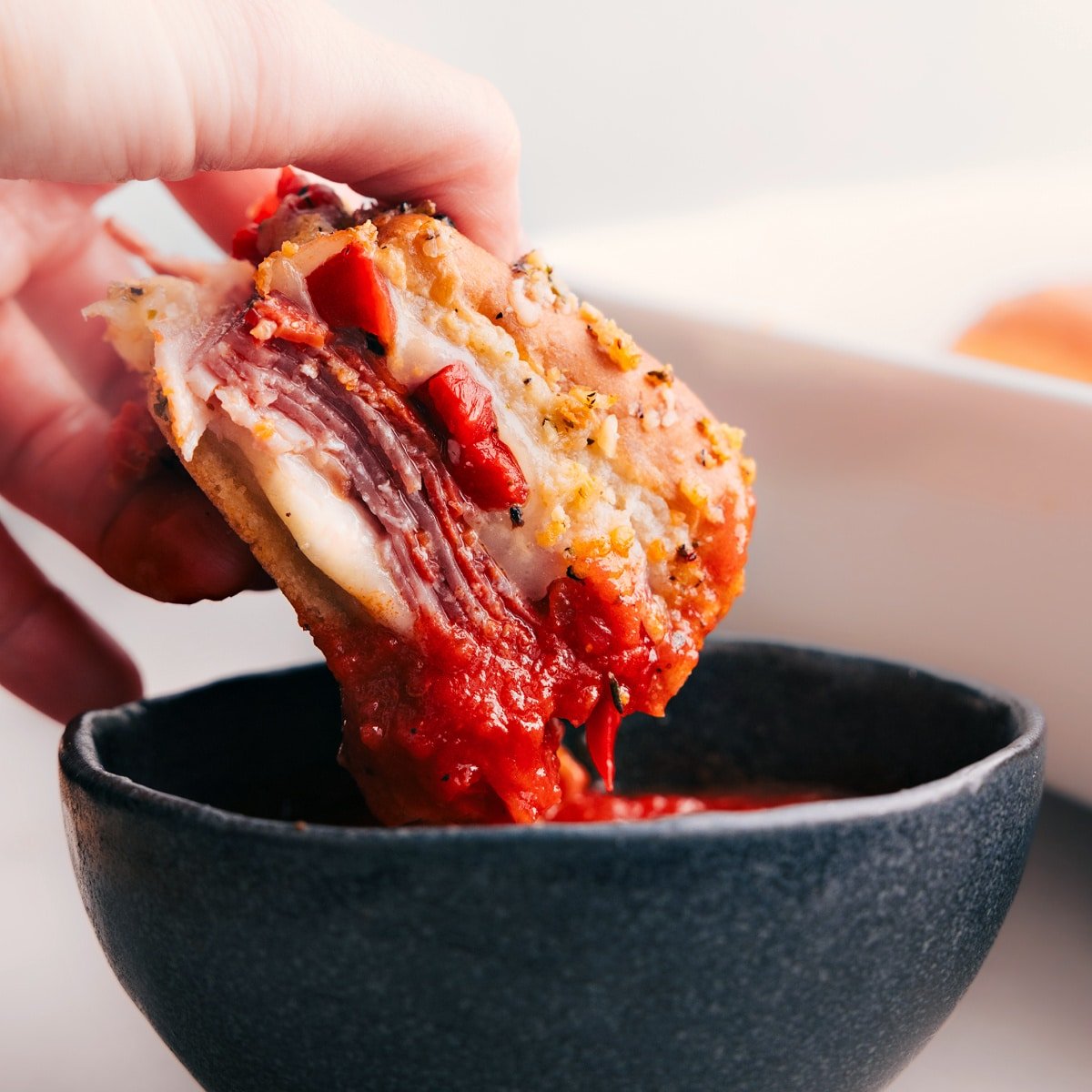 An Italian Slider being dipped in marinara sauce.