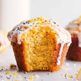 Lemon poppy seed muffin with a fresh bite mark, revealing its moist interior, and adorned with creamy frosting.